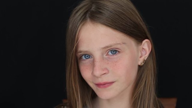 Beautiful blond young girl with freckles indoors on a black background, close up portrait