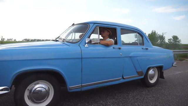 Classic old car traveling on highway on summer day. Young couple driving on country road in vintage automobile. Trip at the retro auto. Concept of summer vacation or holiday. Slow motion Close up
