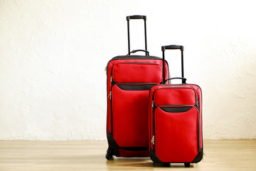 Two colorful red suitcases of same kind different size with telescopic handle up on wooden floor, white wall background. Family trip concept. Packed traveling luggage ready to go. Close up, copy space