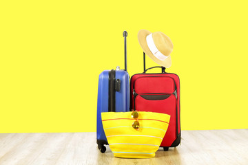Red textile suitcase & blue hard shell luggage, extended telescopic handle, straw hat, yellow beach bag, mirrored sunglasses, yellow wall background. Couples retreat trip concept. Close up, copy space