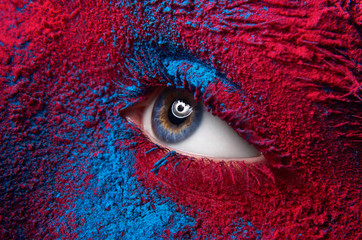 Macro en close-up creatief make-upthema: mooi vrouwelijk oog met droog verfstofpigment op gezicht, rode en blauwe kleur
