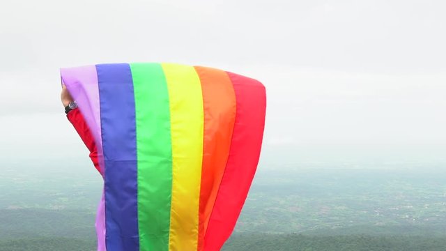 man waving rainbow flag LGBTI symbol flag on mountain top slow motion shot at 120 fps