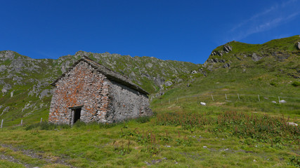 Fototapeta na wymiar Casa in sasso circondata dal prato verde e dal cielo blu in alta montagna in estate