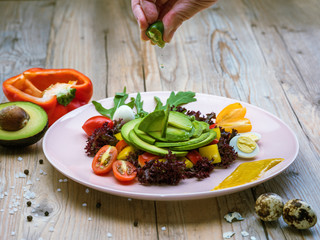 Avocado salad with cherry tomatoes, red and yellow pepper, quail eggs, lettuce and piece of lime in human hand. Avocado is source of nutrition, vitamins, popular food for sport and health diet.