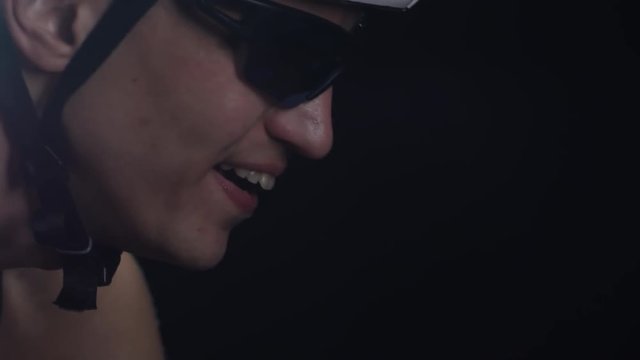 PAN with close up of tired professional cyclist in sunglasses and protective helmet breathing hard and riding bicycle against black background