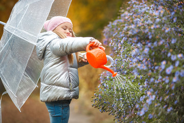 Little girl watering the flowers in the garden in the autumn