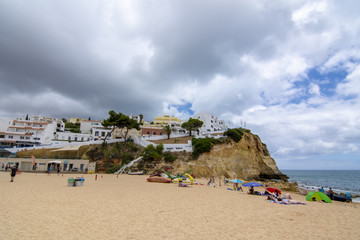Obraz premium turistas en la playa del pueblo de Carvoeiro con coloridas casas, región de Algarve, Portugal
