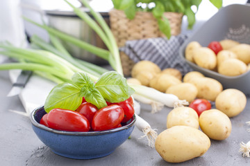 Fresh green onions, young potatoes, cherry tomatoes and green basil. Healthy food and vitamins. Preparation of lunch. Summer seasonal vegetables. Copy space.