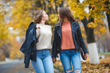 Young pretty girls having fun outdoors in autumn background. Cheerful friends in the fall time