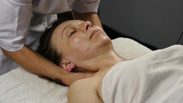 female doctor doing anti-aging massage to client. woman enjoys plastic face massage in spa saton. slow motion