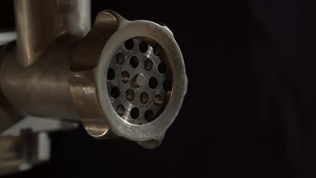 Grid of working meat grinder in dark wall background, close-up view. Modern electrical devices for cooking in home conditions and professionals