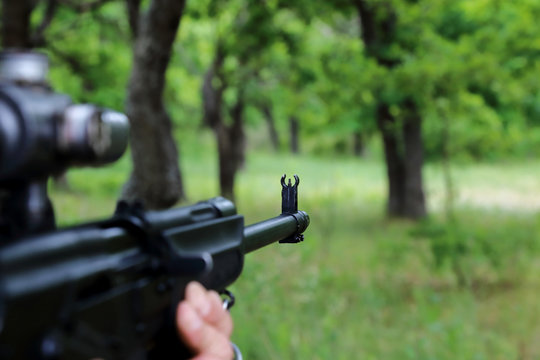 The hunter is aiming at the gun. Sighting the gun barrel at the target.