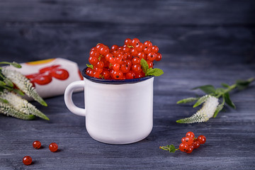 Ripe red currant berries in a white cup and flowers on a dark background