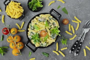 Fusilli pasta with spinach, cherry, bacon in black dishes. Garnished with fresh spinach