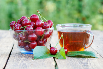 Red ripe cherry fruits with peduncles in glass bowl and cup of tea