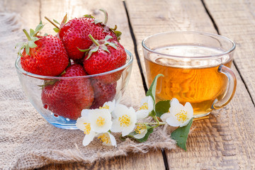 Strawberries in glass bowl and glass cup of green tea with jasmine flowers