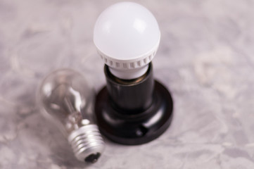 One modern new plastic led electric bulb in black socket near old glass bulb on old worn gray concrete floor