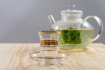 Empty tea glass in front of a teapot filled with peppermint tea