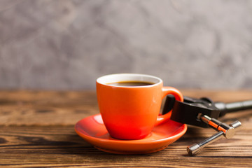 Black metal arm holds orange ceramic mug full of black coffee on old wooden brown table with copy space for your text