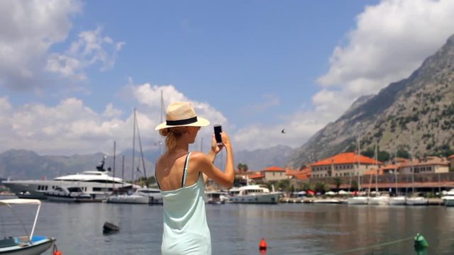 slender girl takes pictures on the phone of a mountain bay with yachts