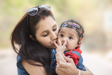 Happy mother kissing her 5 month daughter in the park. selective focus, shallow depth of field.