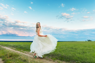 Young blonde woman bride spinning outdoors on fild