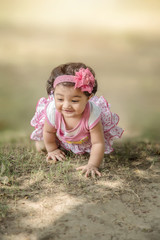 Selective focus of Happy 6 month Indian/Asian little kid wearing pink dress crawling on the grass and playing. shallow depth of field.