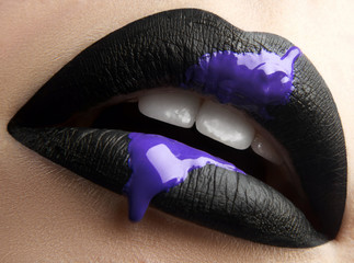 Naklejka premium Macro and close-up creative make-up theme: beautiful female lips with black lipstick and purple liquid paint.