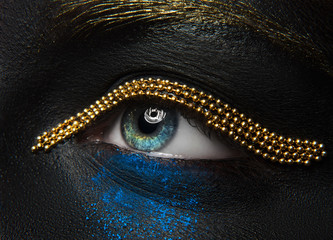 Macro and close-up creative make-up theme: beautiful female eyes with black skin with a gold chain...