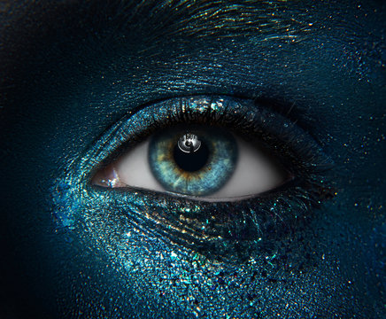 Macro and close-up creative make-up theme: beautiful female eyes with black skin with a blue-green pigment sparkles