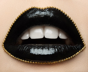 Macro and close-up creative make-up theme: beautiful female lips with black lipstick and a gold chain along the contour