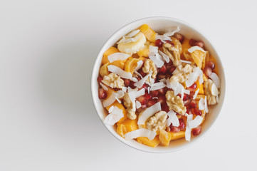 Bowl with fresh fruits: mango, banana, tangerine, pomegranate seeds, coconut flakes, walnut and dried apricot. Healthy salad