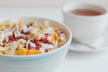 Bowl with fresh fruits and nuts served with a cup of herbal hot drink. Mango, banana, pomegranate seeds, coconut flakes, tangerine and walnut. Healthy dessert
