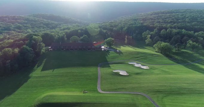 Aerial camera pushing in towards a large lodge with a mountain behind it and the sun setting against it.