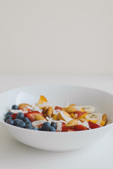 Vertical photo of healthy breakfast with oats, blueberry, peach, strawberry, almond, banana and coconut. Healthy and balanced meal with healthy carbs