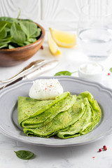 Green thin pancakes with spinach, poached egg, sour cream, lemon and aromatic herbs, delicious healthy food