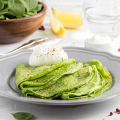 Green thin pancakes with spinach, poached egg, sour cream, lemon and aromatic herbs, delicious healthy food