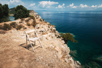 Free empty wooden chair standing on the rocky cliff with beautiful sea view. Sunny summer day in Greece