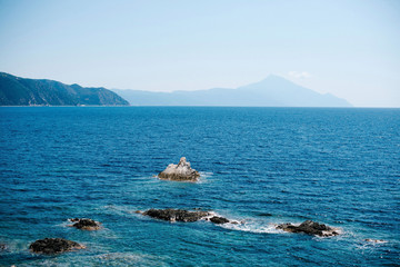 Top view of beautiful mediterranean sea and small rocky island on sunny summer day in Greece. Mountains in background