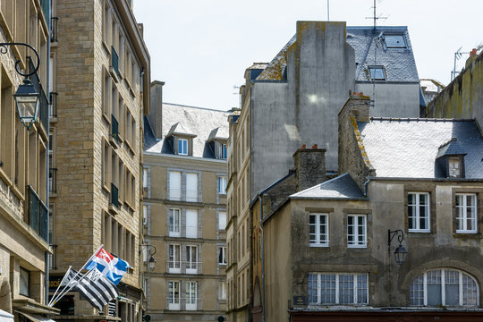 Various types and generations of residential buildings made of granite masonry and slate rooftops in the old town of Saint-Malo, France, with the flags of the city and Brittany blowing in the wind.