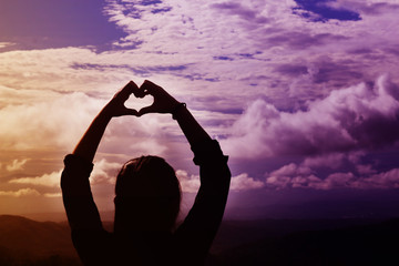 Back or rare view women do hand symbol of heart in fantasy dreamy violet and orange light wide sky