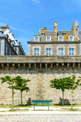 View of the surrounding wall of the city of Saint-Malo, France, a small park with trees and benches at the foot of the wall and granite residential buildings sticking out above the rampart