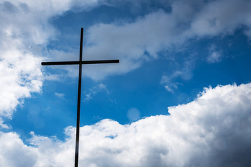 Silhouette of wooden cross with a bright blue sky and sun