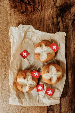 Swiss bread buns called in German 1. Augustweggen baked in Switzerland to celebrate Swiss National Day on August 1st. Swiss flag with white cross on red background.