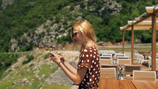 stylish woman with a phone stands in a cafe on a background of mountains