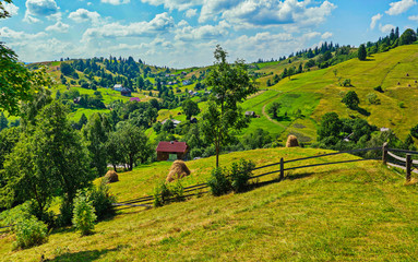 Obraz premium A picturesque plain with huts and haystacks against the background of green mountains and blue sky
