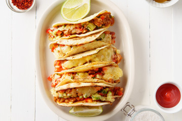 Mexican tacos with chili con carne and grated cheese served on a plate over white wooden table