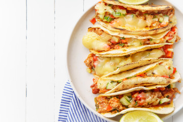 Mexican tacos with chili con carne and grated cheese served on a plate over white wooden table