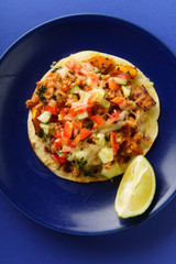 Overhead image of mexican tacos with chili con carne, sweet potatoes and grated cheese served over a blue background