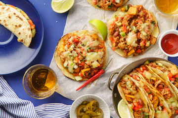 Overhead image of mexican tacos with chili con carne, sweet potatoes and grated cheese served over a blue background